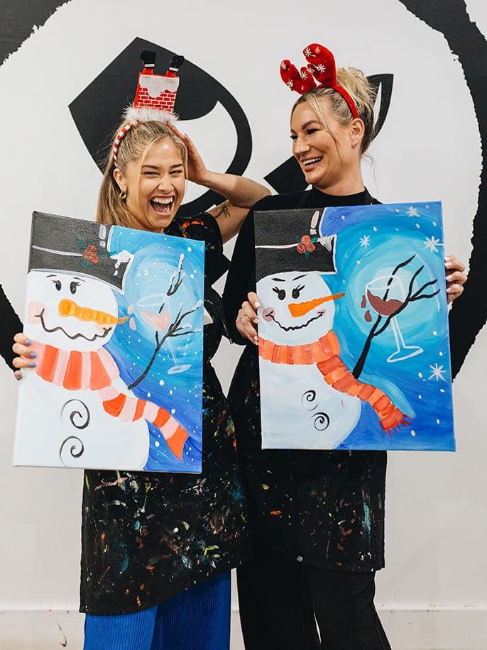 two women holding their paintings of a snowman at Pinot & Picasso