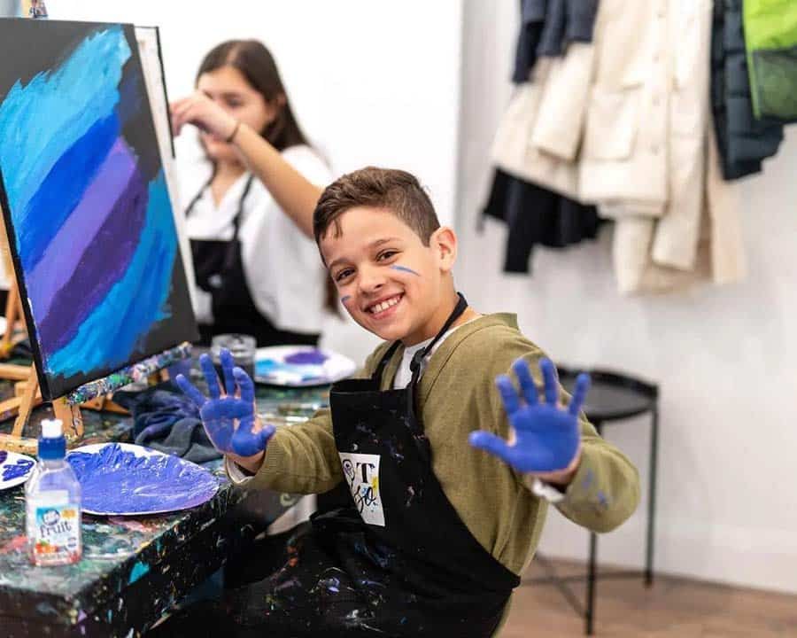 a boy with an apron on and his hands covered in paint from creating an artwork at Pinot & Picasso