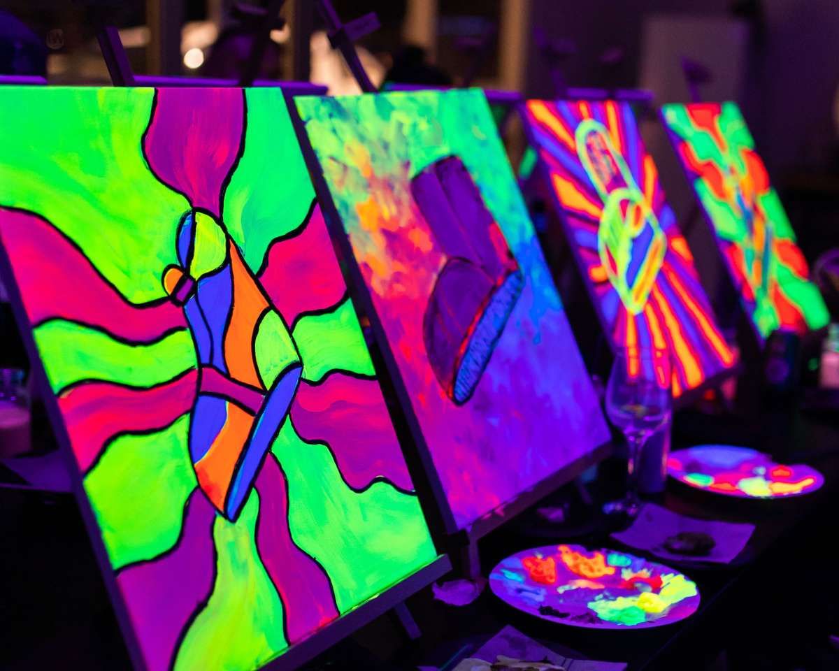 four artworks of different shoes are glowing with flourescent paint under UV purple light at Pinot and Picasso