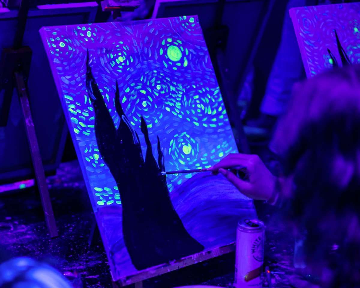 a woman painting one of Pinot and Picasso's Neong Night Van-Glow artworks with glow in the dark paint
