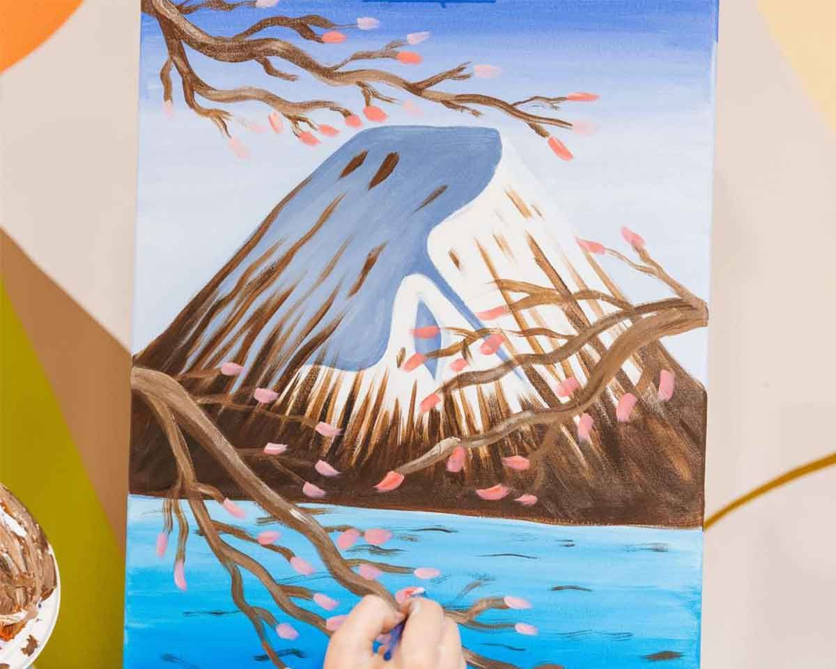 a person painting an artwork of Mount Fuji in Japan with cherry blossoms in the front