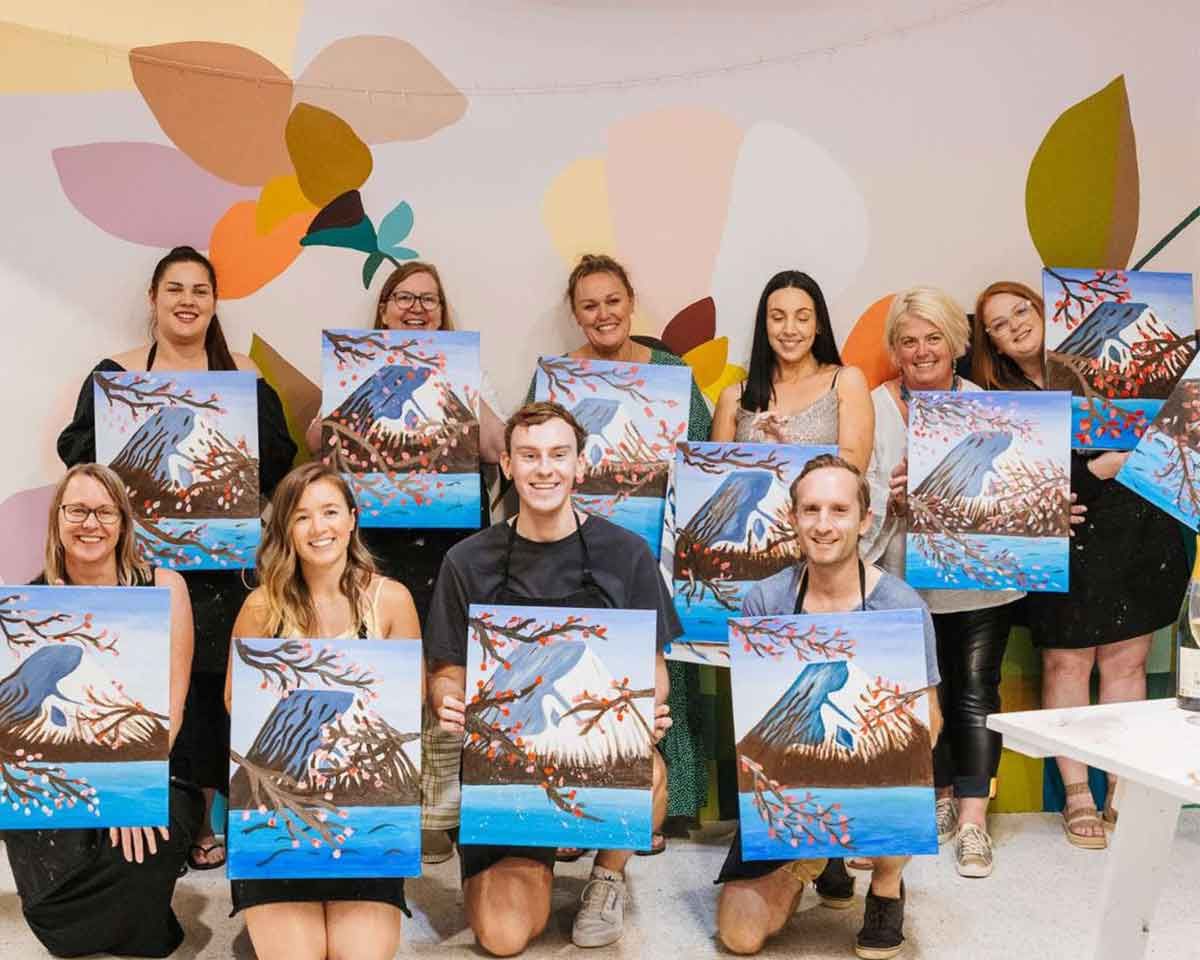 A group of people at Pinot and Picasso posing with their paintings of Mount Fuji