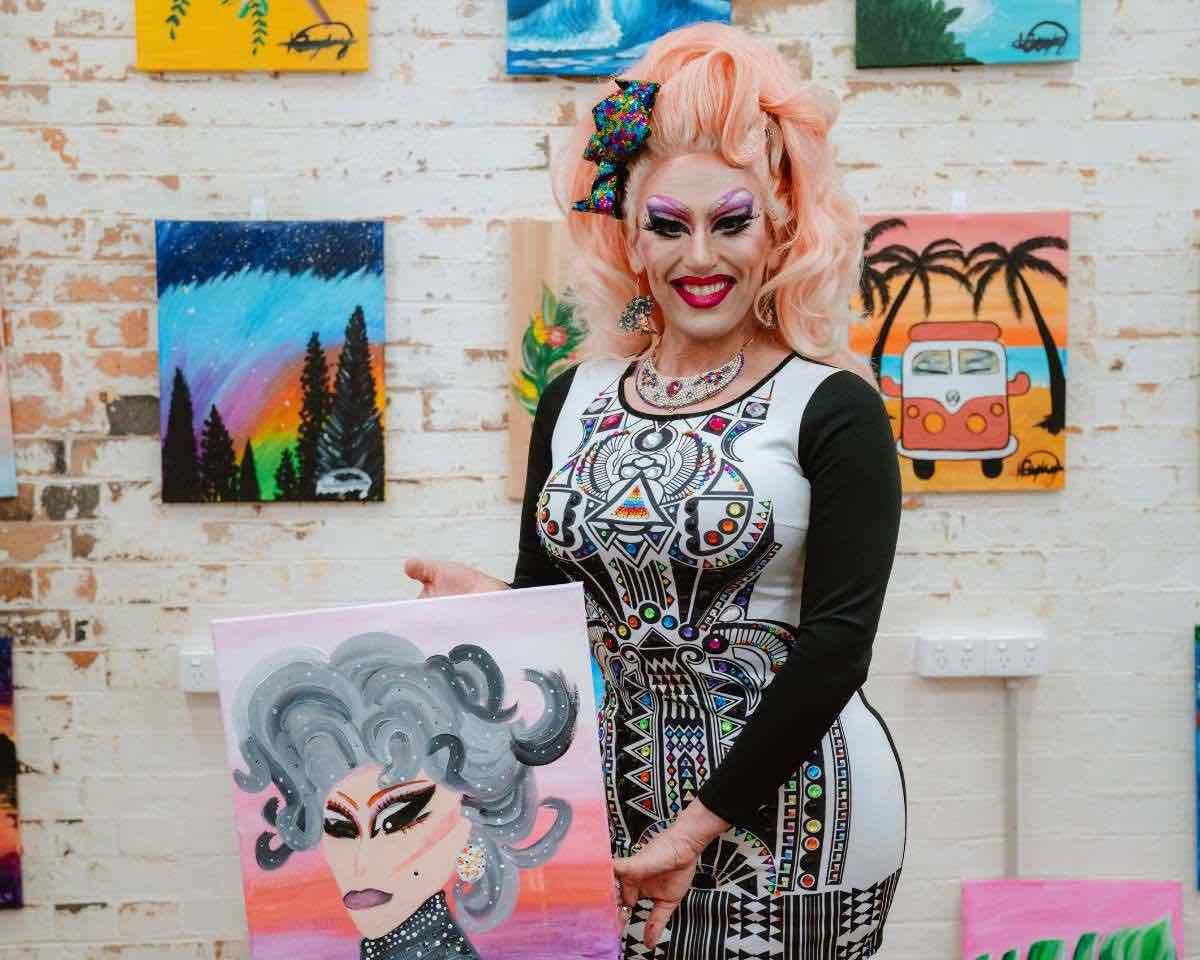 A drag queen holding a painting a special drag queen event at Pinot & Picasso