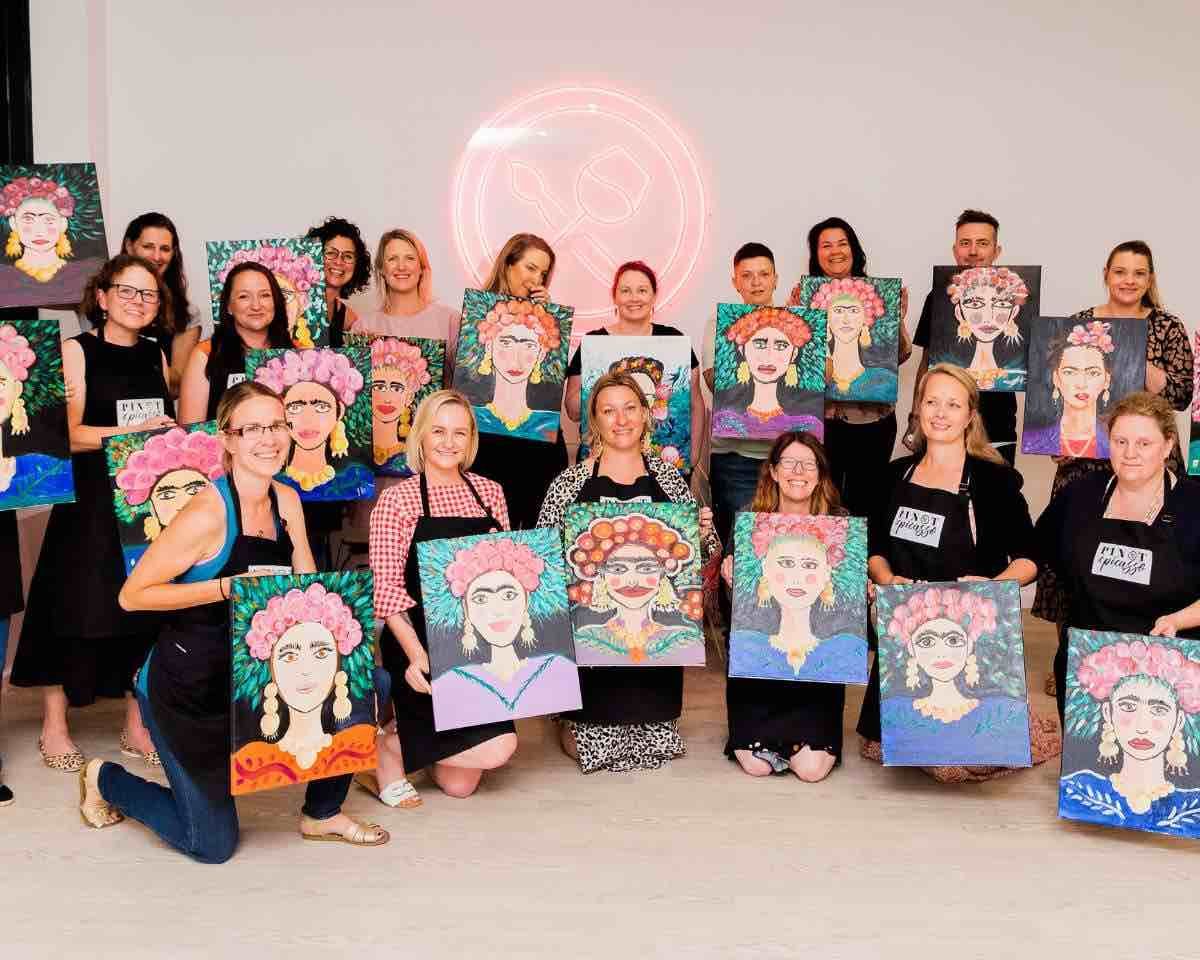 a group of happy people holding their artworks of frida kahlo at Pinot & Picasso paint and sip class
